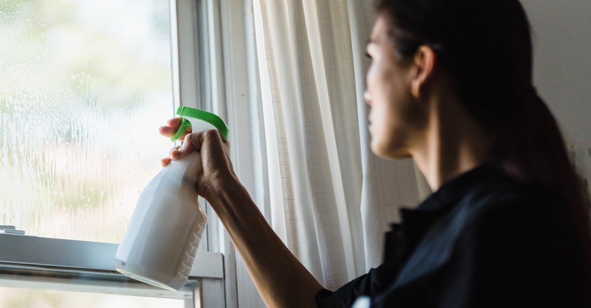 A woman using a spray bottle to clean a glass window inside a room, captured in a close-up shot.