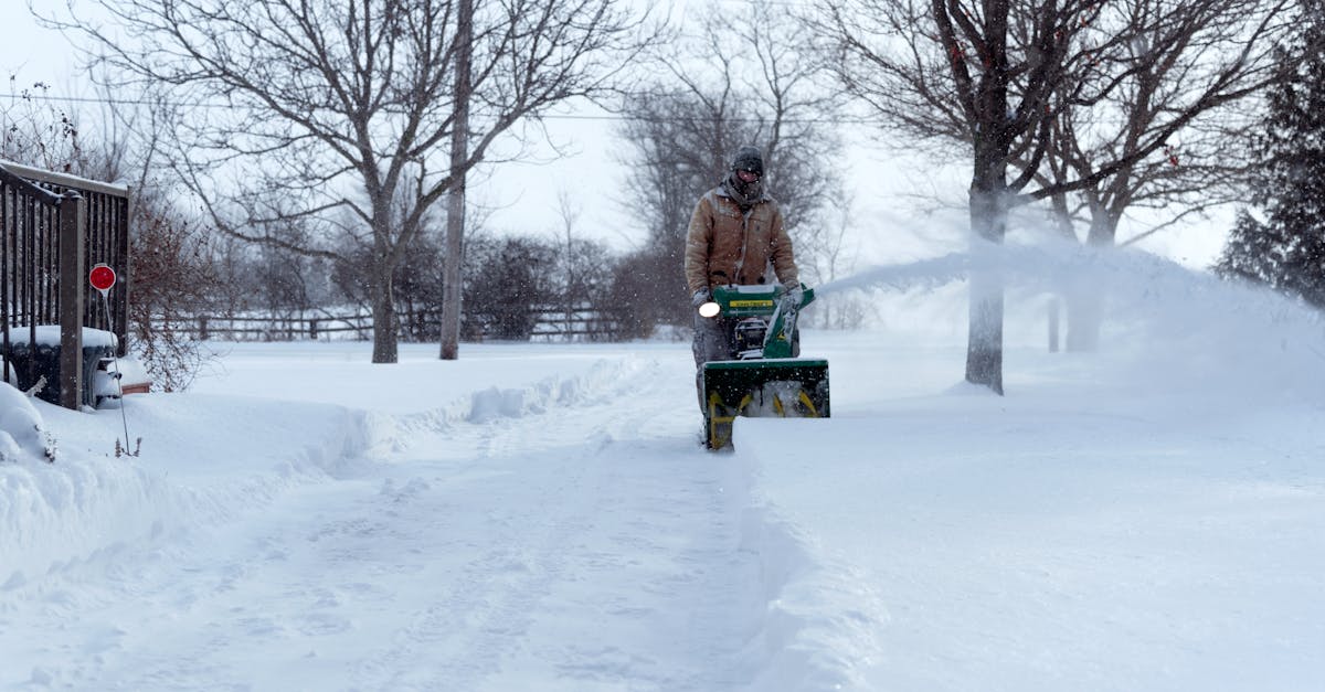 A person operates a snowblower on a snow-covered driveway in Essex, Ontario, during winter.
